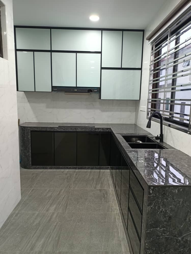 A pale grey glass-fronted kitchen with a dark stone worktop and an L-return under a window.