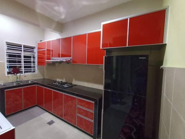 A red gloss kitchen with a black worktop, a hob and a dark fridge, photographed in a home with window grilles.